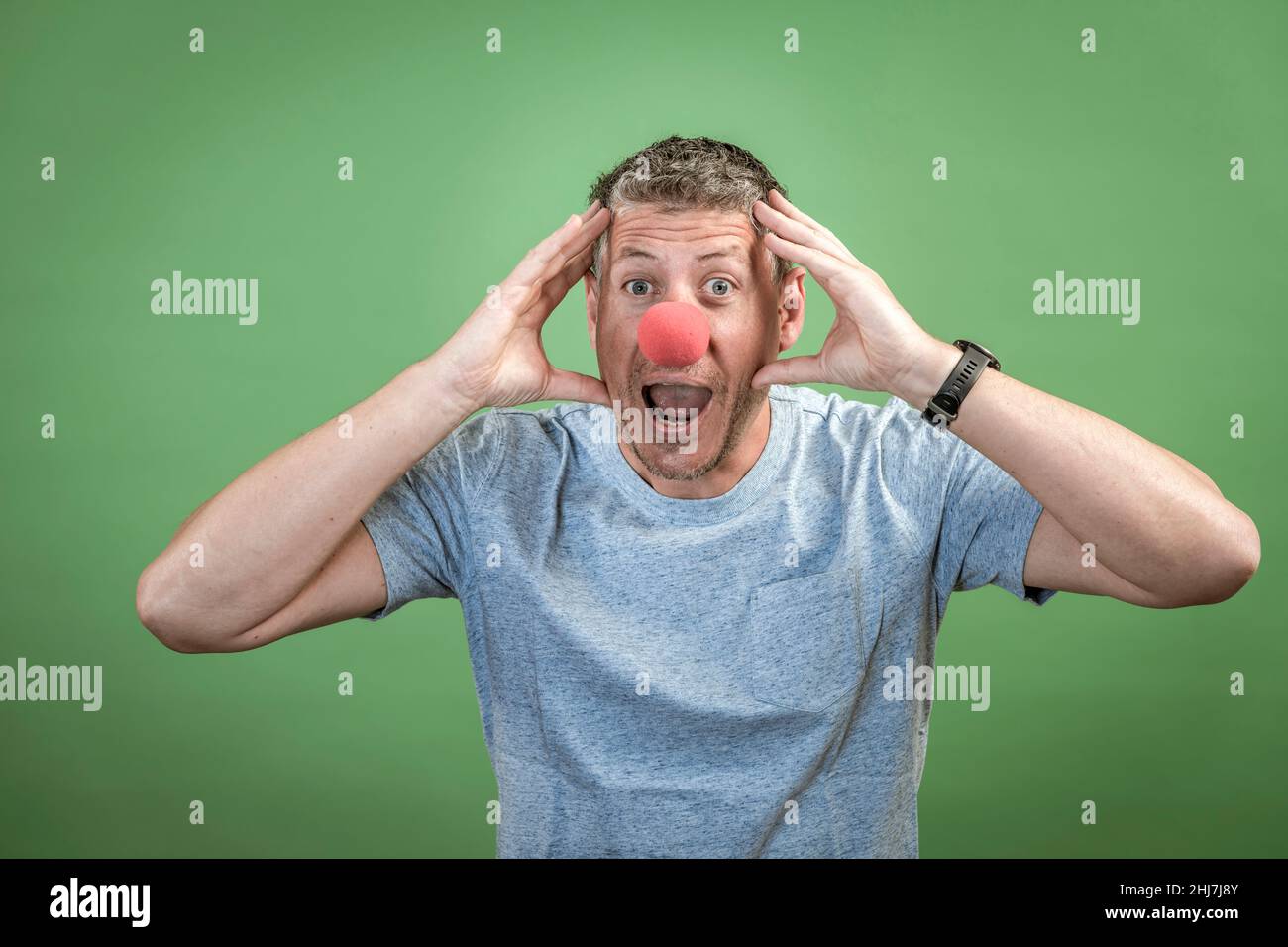 Mann mit roter Clownsnase und grauem Hemd vor grünem Hintergrund Stockfoto