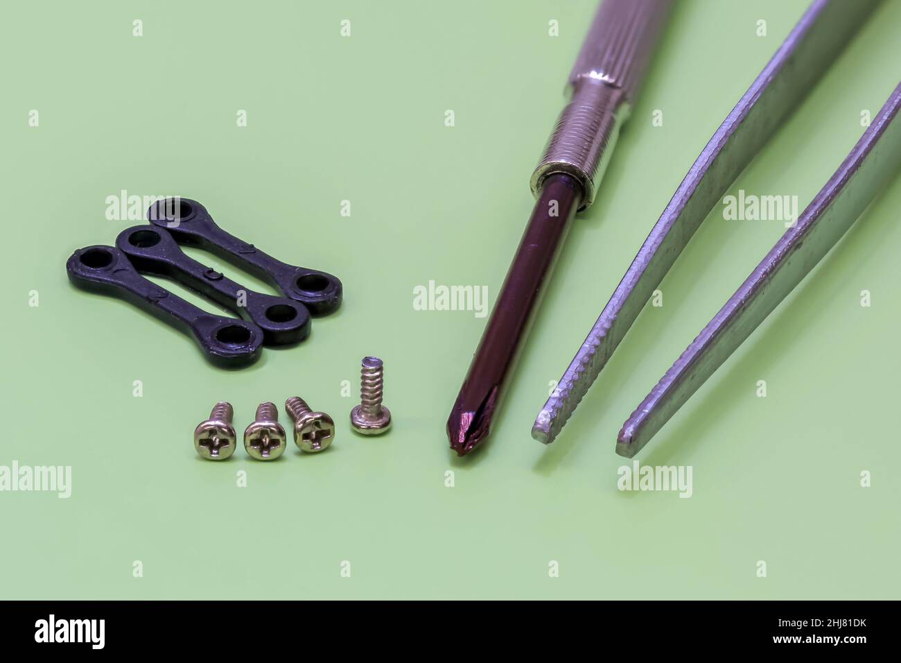 Nahaufnahme von drei Miniatur-Nylonlenkern, Miniaturschrauben, Schraubendreher und Pinzette auf grünem Hintergrund Stockfoto