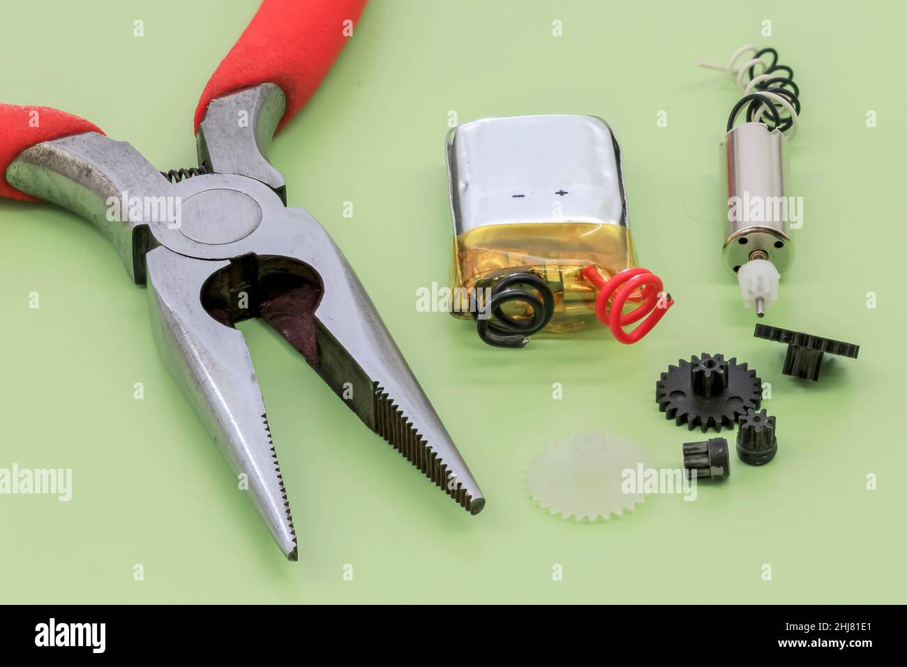 Nahaufnahme eines Miniatur-Elektromotors, Batterie und einer langen Spitzzange auf grünem Hintergrund Stockfoto