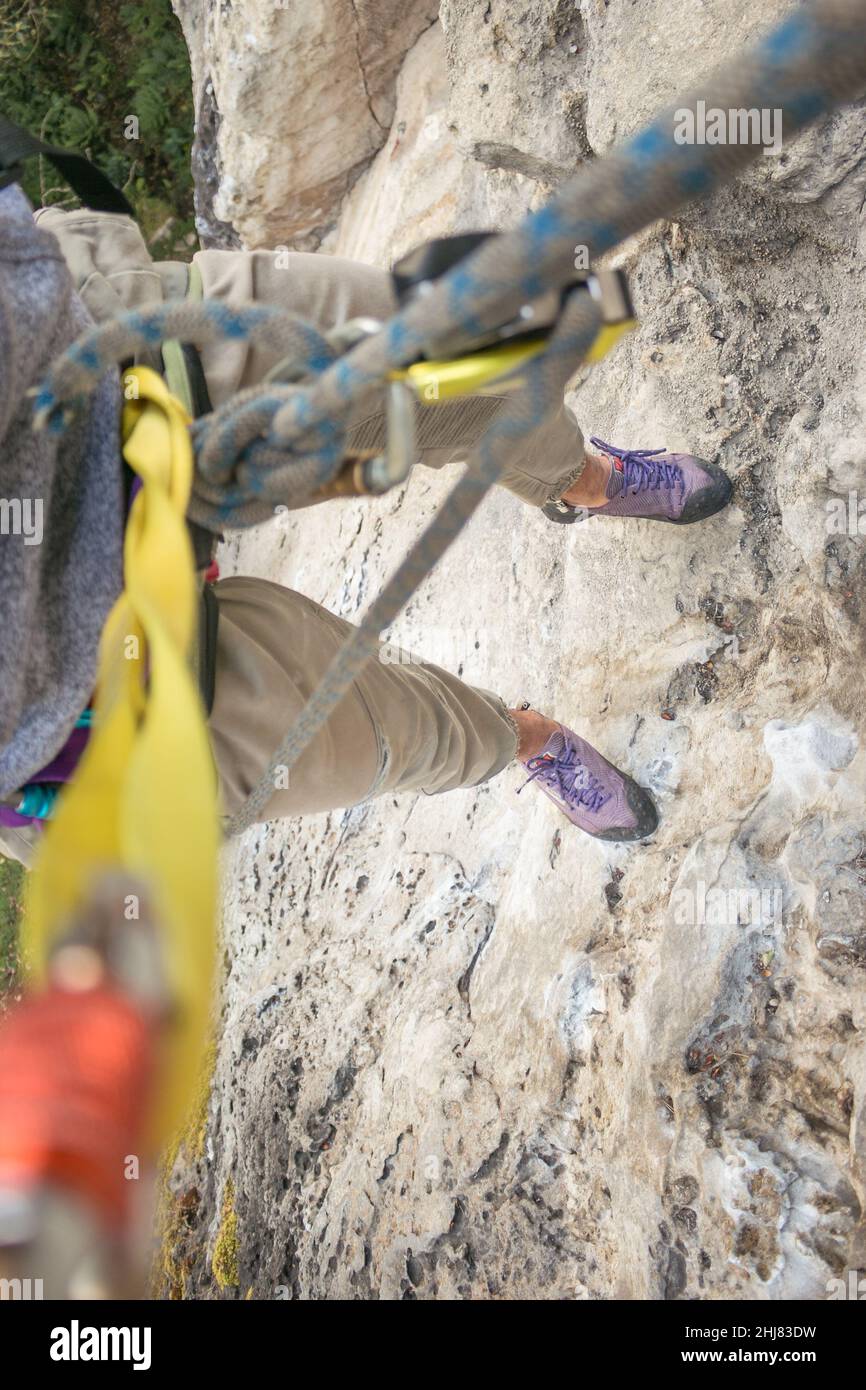POV: Felskletterer hängt am Seil und ragt hoch über dem Boden Stockfoto