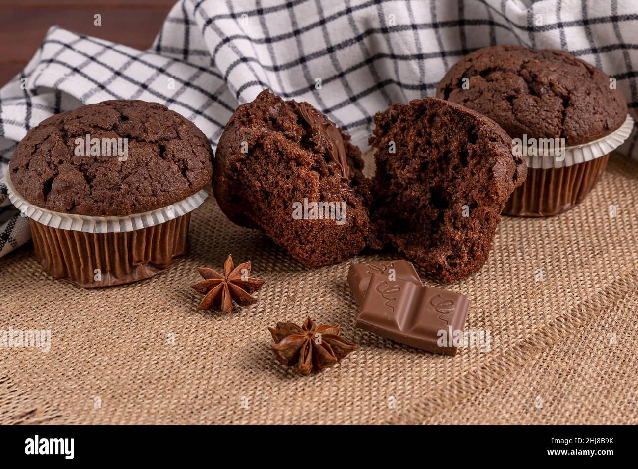 Köstliche Schokoladen-Muffins mit quadratischer Schokolade und Sternanismuffins auf Jute-Matte Stockfoto