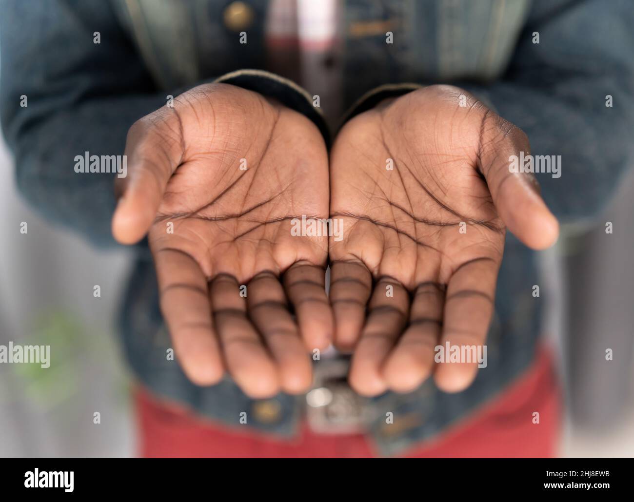 Nahaufnahme eines jungen afroamerikanischen Mannes mit Jeansjacke. Bettelhände eines armen Mannes Konzept. Junger afroamerikanischer Mann mit ausgestreckten Händen bettelt um Geld für das Leben. Stockfoto
