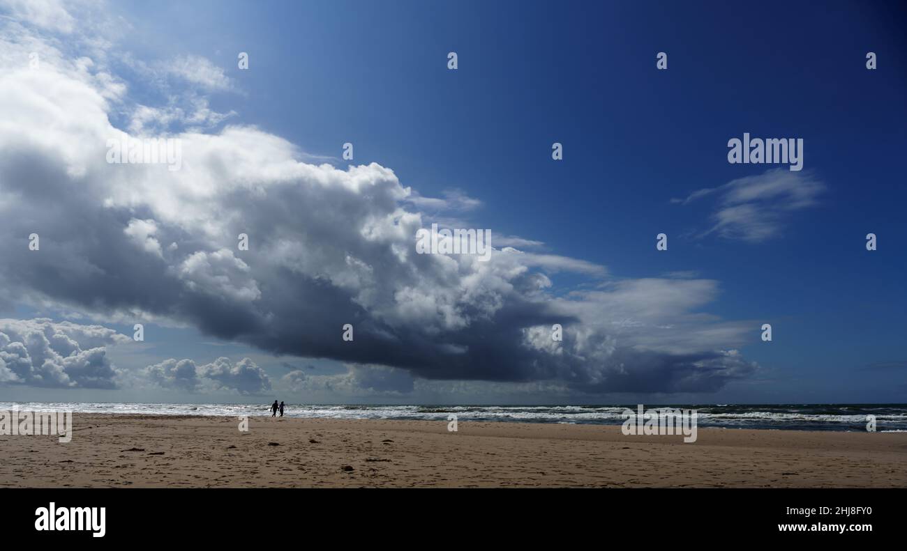 Ein weit entferntes Paar macht im Sommer an der mengenleeren däischen Nordseeküste einen Spaziergang am Wasser vor druckvoller Wolkenformation Stockfoto
