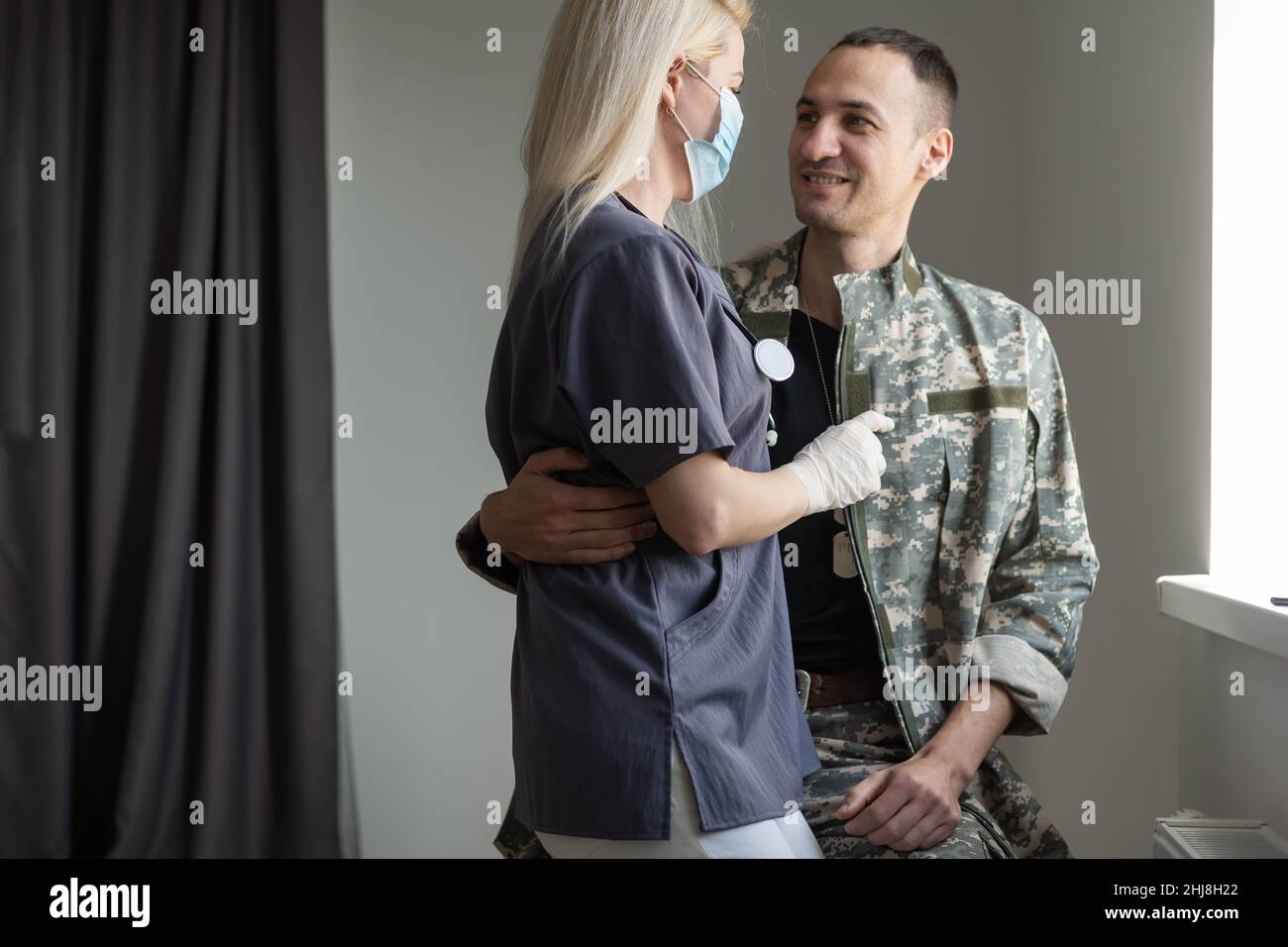 Fürsorgliche Krankenschwester, die die Hände hält und ihren militärischen Ehemann unterstützt, während sie im Krankenhaus mit ihm spricht Stockfoto