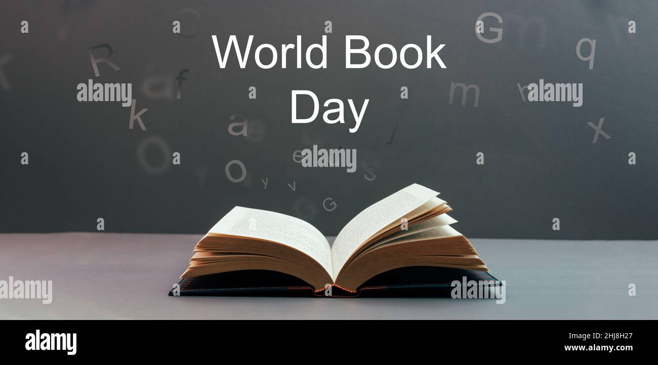 Weltbuchtag, offenes Buch mit Briefen, die auf einem grauen Hintergrund mit dem Text Weltbuchtag auslaufen. Stockfoto