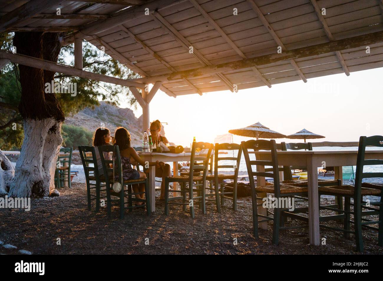 Familie genießt das Abendessen in einem Restaurant am Strand bei Sonnenuntergang. Menschen in einem Café an einer wunderschönen Strandtaverne mit Blick auf den Sonnenuntergang auf den Sfinari Strand in C Stockfoto