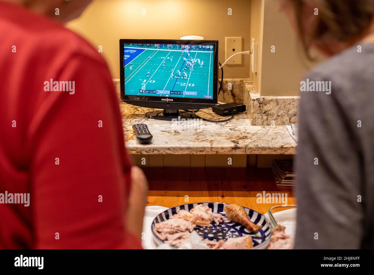 Zwei Personen schauen Fußball im Fernsehen, während sie das Thanksgiving-Abendessen vorbereiten. Stockfoto