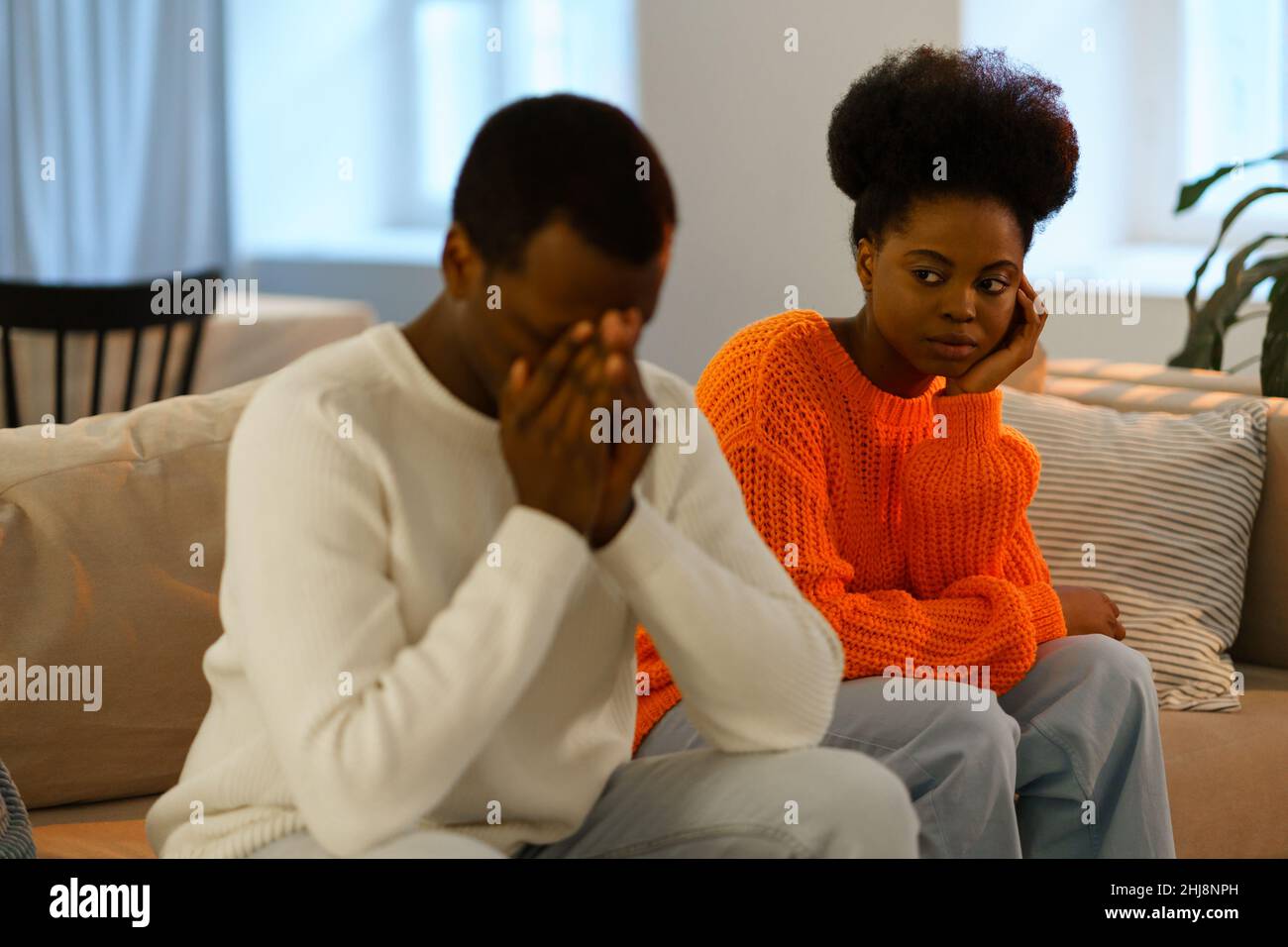 Missverständnisse in Liebesbeziehungen. Trauriges afrikanisches Familienpaar, das nach einem Konflikt auf dem Sofa sitzt Stockfoto