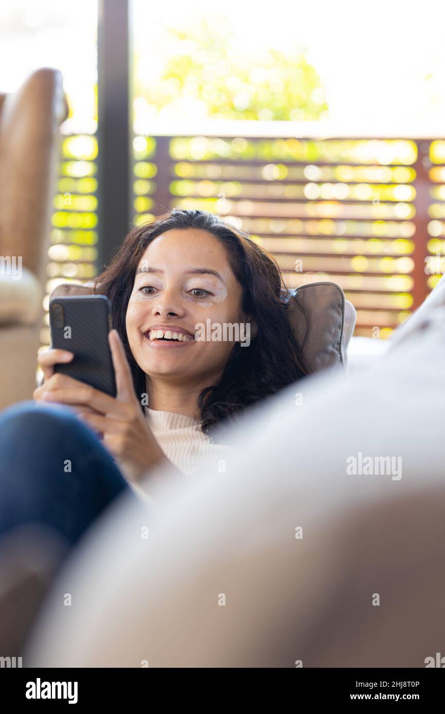Fröhliche Biracial junge Frau mit Smartphone, während sie sich auf dem Sofa zu Hause entspannen, Platz kopieren Stockfoto