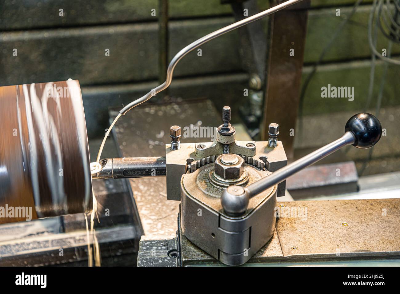 Der Meißel einer Drehmaschine zermahlt ein Stahlrohr, das durch den Strom einer Kühlflüssigkeit abgekühlt wird Stockfoto