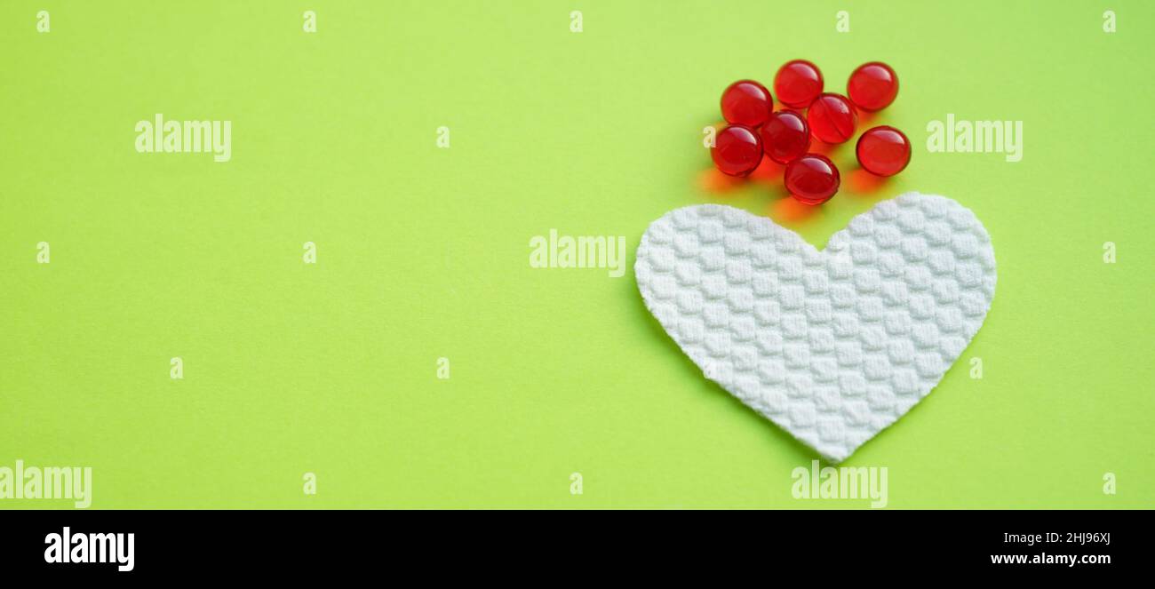 Rote Kapseln und weißes Herz auf einem grünen Tisch. Stockfoto
