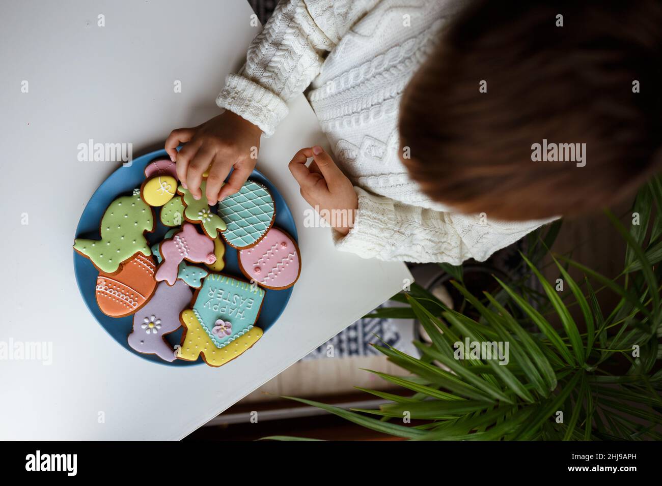 Ein Kind in den Händen hält einen Teller mit Ostereiern, Hase, Huhn und Haus aus hausgemachten Keksen. Stockfoto
