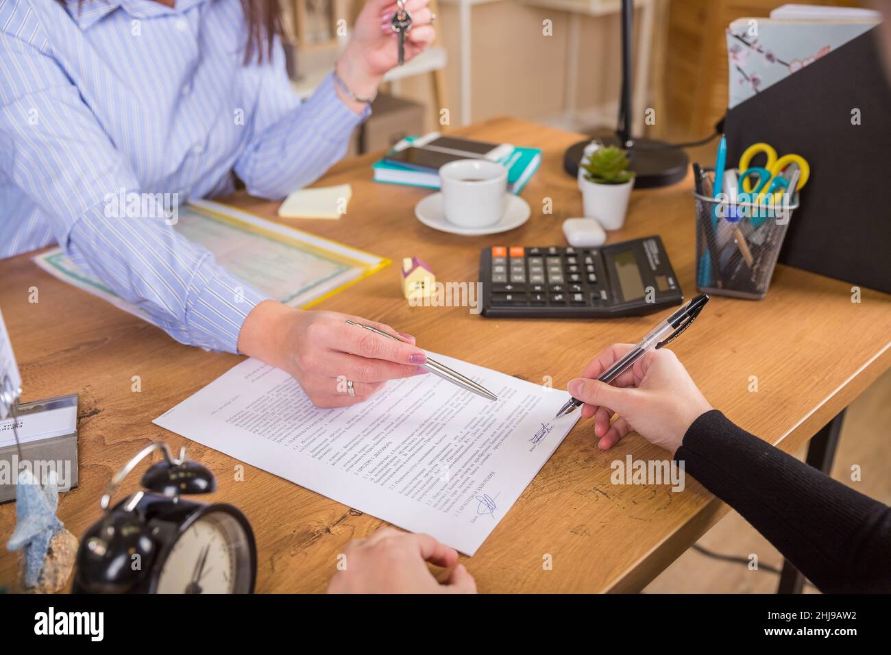 Der Kunde unterzeichnet ein Dokument über die Immobilienaktivität neben einem Anwalt oder einem Immobilienmakler, der am Schreibtisch sitzt Stockfoto