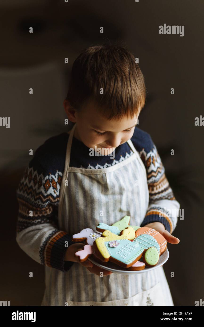 Ein Kind in den Händen hält einen Teller mit Ostereiern, Hase, Huhn und Haus aus hausgemachten Keksen. Stockfoto