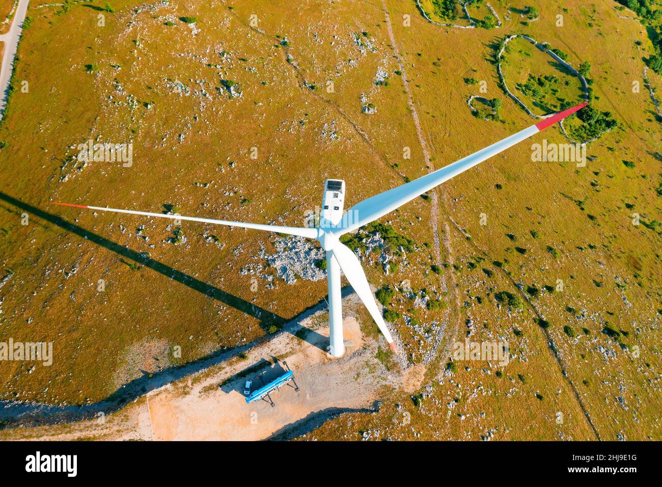 Die leistungsstarke Windenergieanlage mit großen Rotorblättern produziert an sonnigen Tagen auf der Bergspitze saubere erneuerbare Energie und schützt die Umwelt in der oberen Ansicht Stockfoto