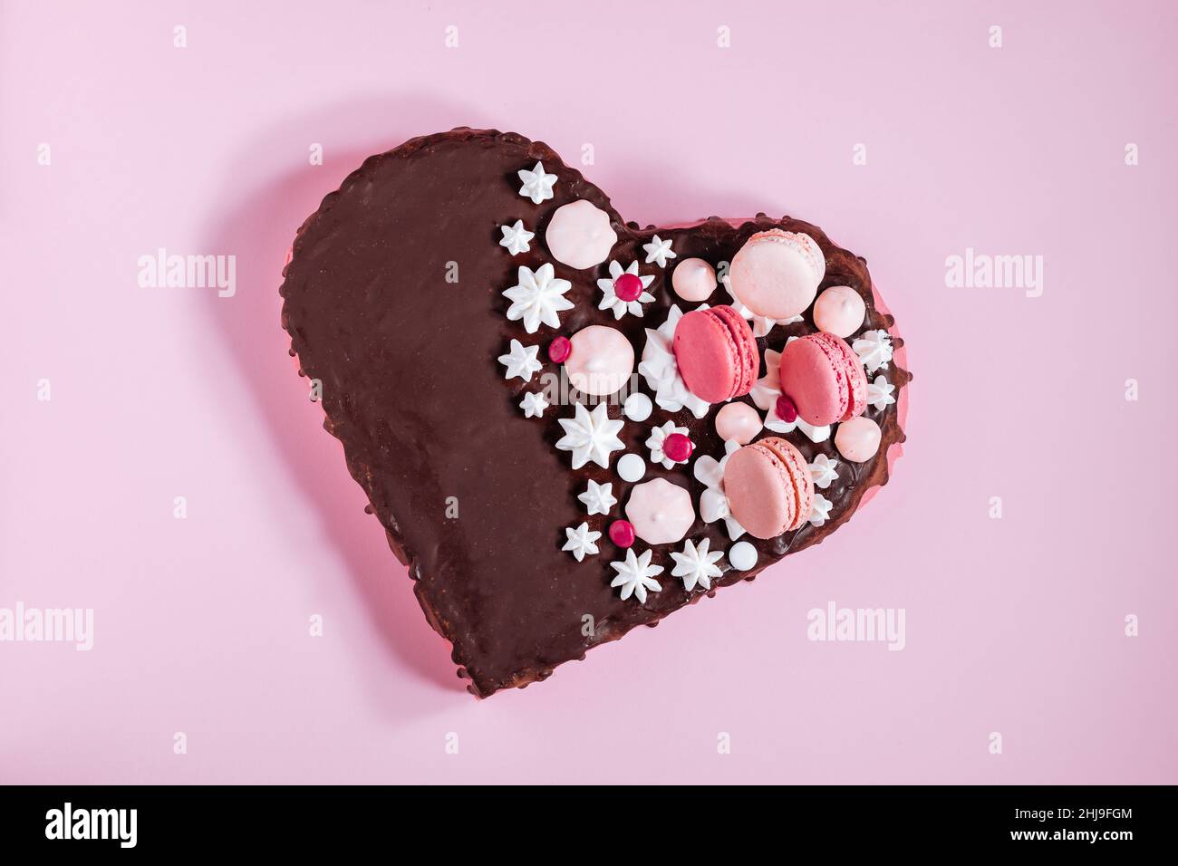 Draufsicht auf Pink Heart Shaped Cake mit Schokoladenglasur, Bagues und Makronen als Dekoration. Valentinstag, Muttertag. Stockfoto