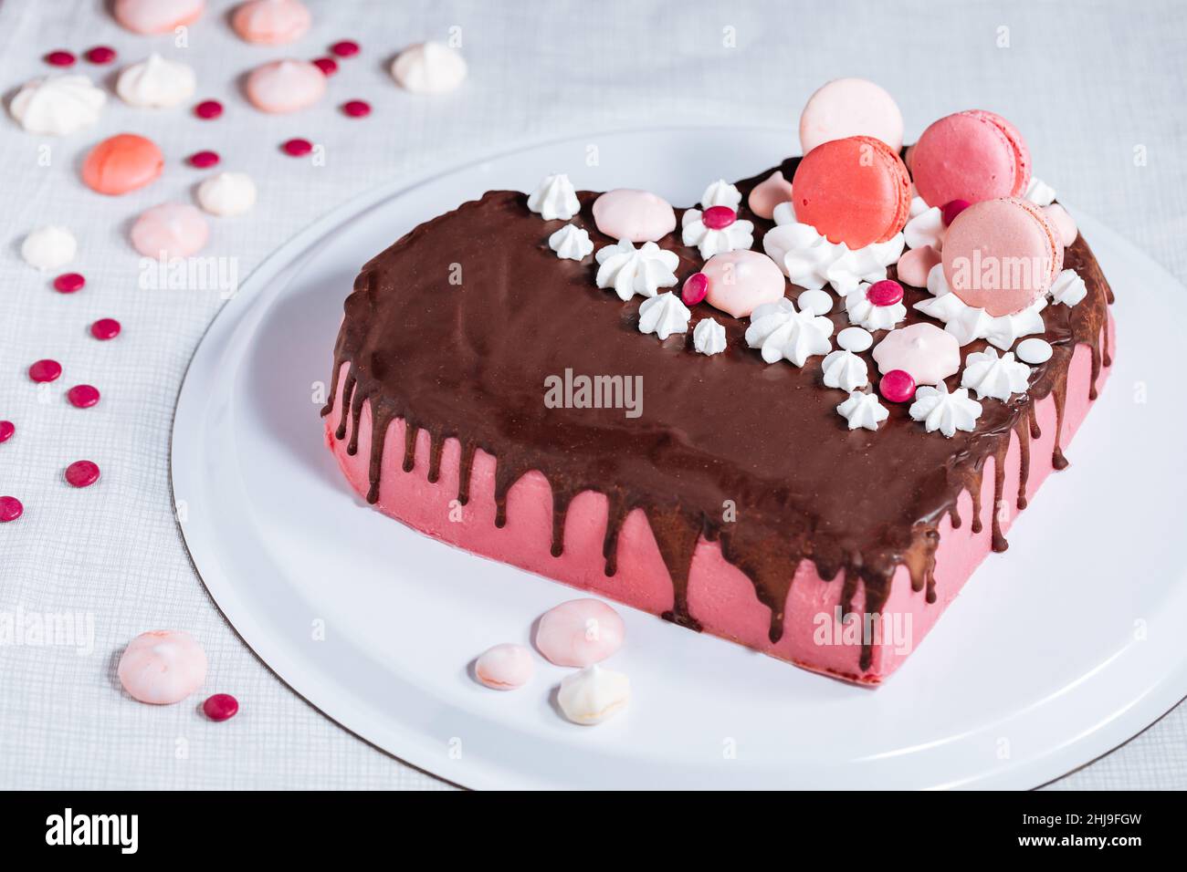 Draufsicht auf Pink Heart Shaped Cake mit Schokoladenglasur, Bagues und Makronen als Dekoration. Valentinstag, Muttertag. Stockfoto