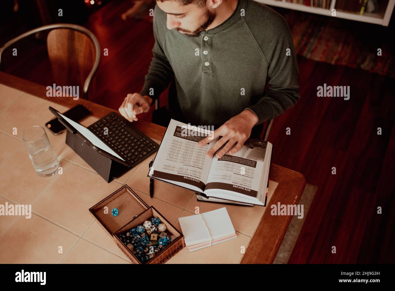 30-etwas Mixed-Rennen fit Mann überprüft seine Tablette als Referenz, während Vorbereitung auf Spiel Master ein Tabletop Fantasy-Rollenspiel mit Freunden, Studie Stockfoto