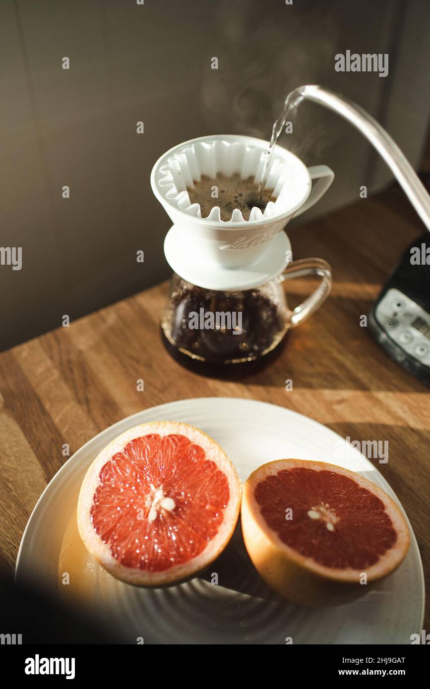 Eine Grapefruit, ein Ei und eine Banane bilden ein Frühstückslächeln auf einem weißen gesprenkelten Teller, umgeben von Utensilien, Kaffee in einem chemex und anderen Früchten Stockfoto