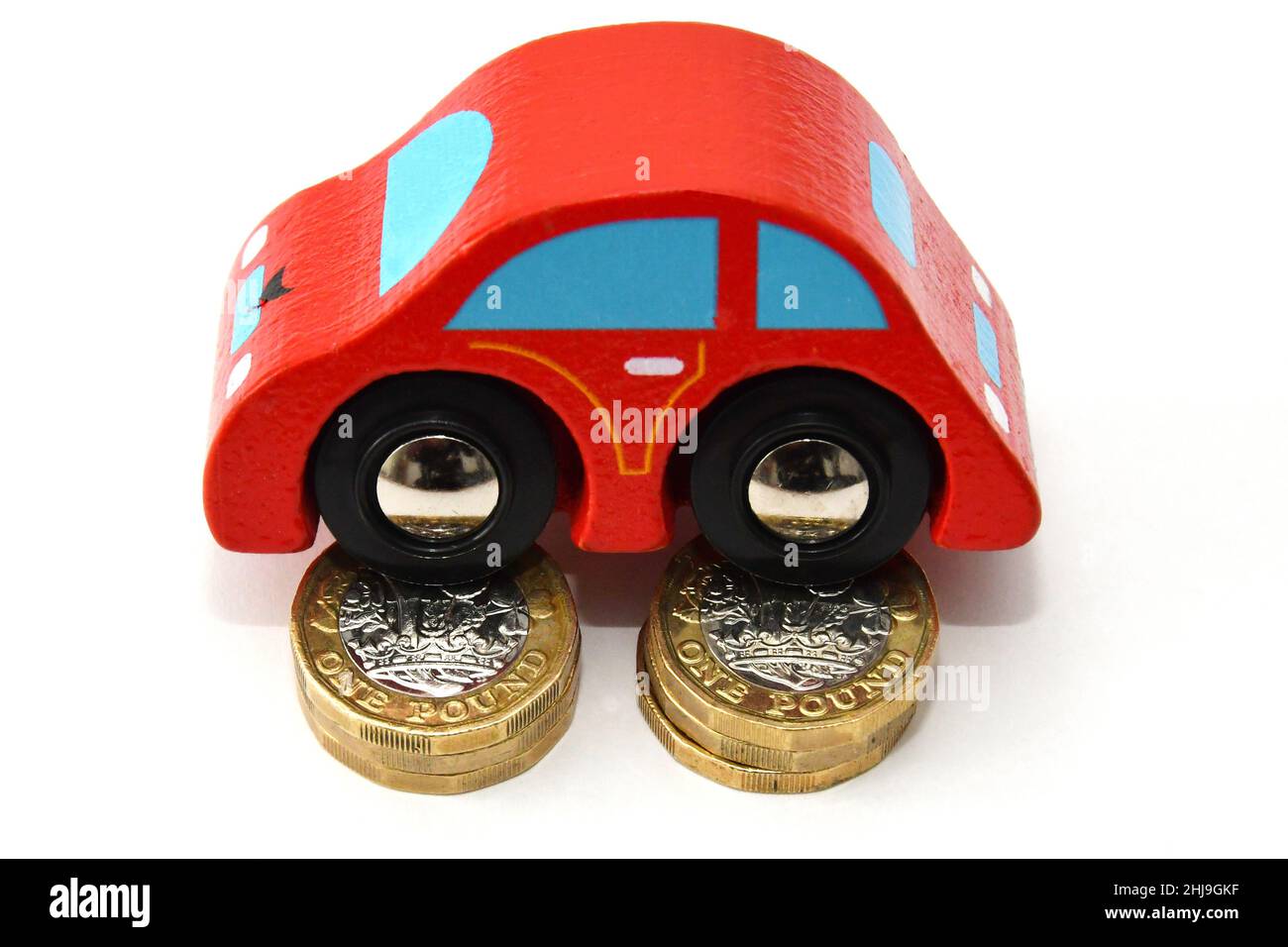 Nahaufnahme eines Modellautos, das auf zwei Säulen von 1-Pfund-Münzen auf einem schlichten weißen Hintergrund liegt. Car Running Costs Konzept. Keine Personen. Stockfoto