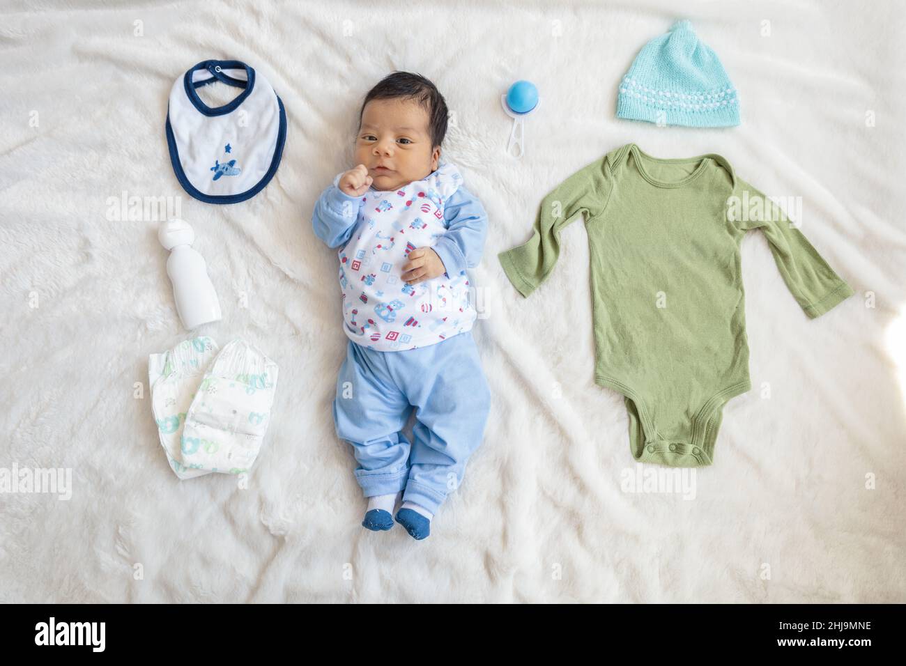 Ganzkörper eines Babys, das neben Babykleidung wie Hut, Lätzchen, Body, Kinderzubehör, Neugeborenenmode und -Lifestyle, Studio liegt Stockfoto