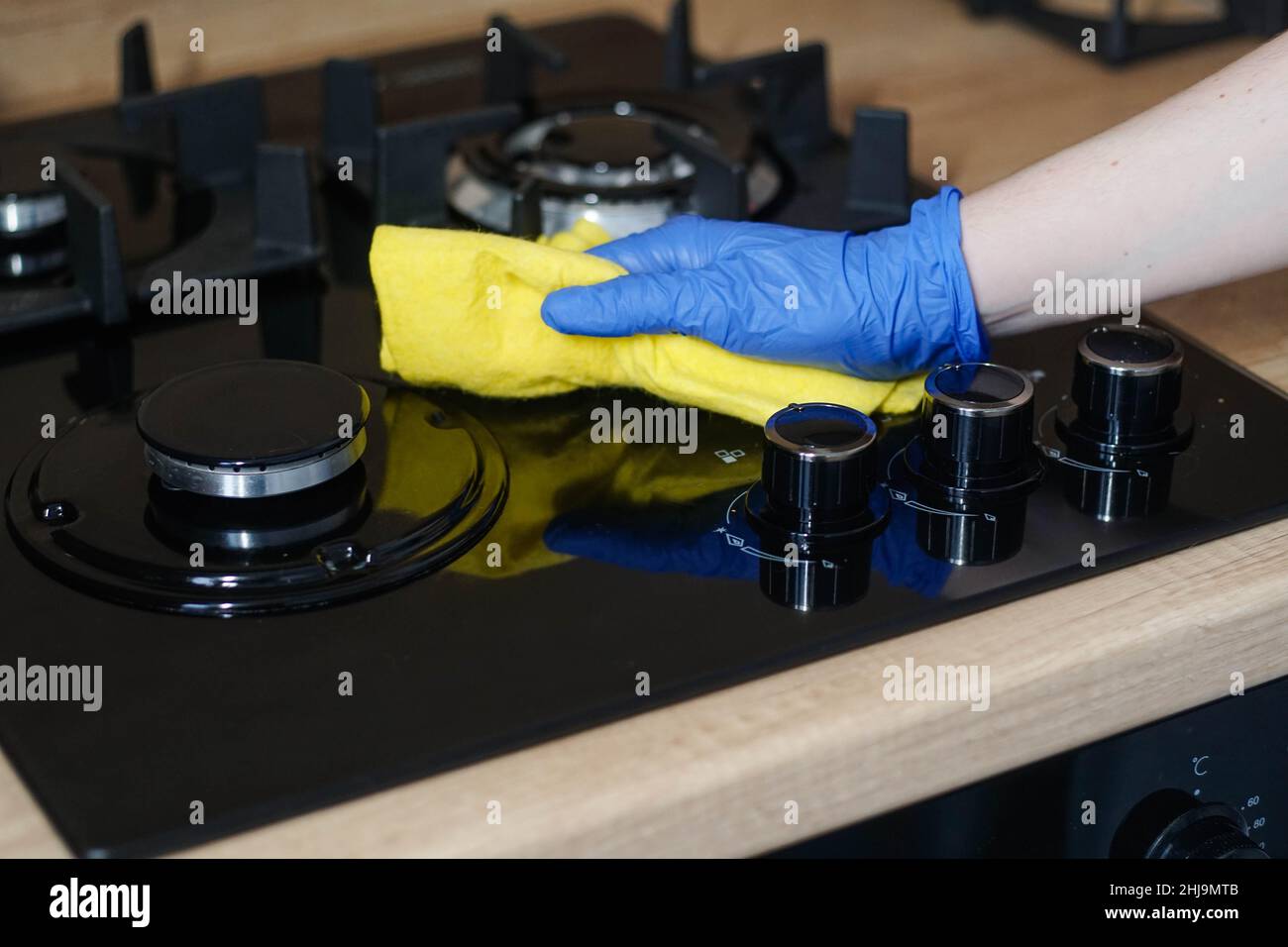 Gasherd wird gereinigt. Frauenhand in Gummihandschuh Polieren schwarze Glasoberfläche mit gelben Lappen. Stockfoto