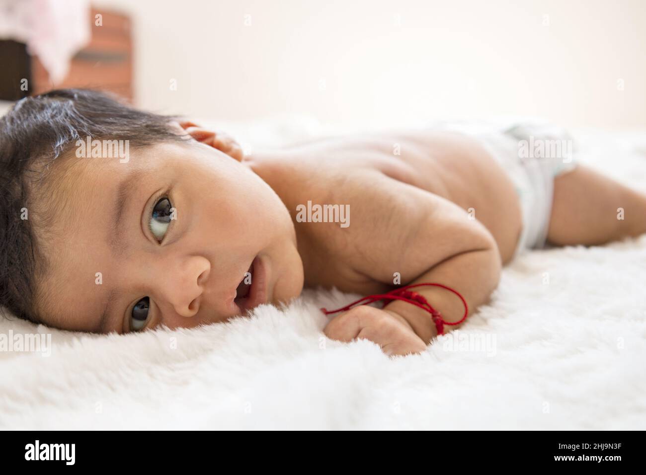 Schönes Baby, das auf dem Bauch liegt, mit Windel und rotem Armband, vollem Säuglingskörper, neugeborenem Lebensstil, Unschuld Stockfoto