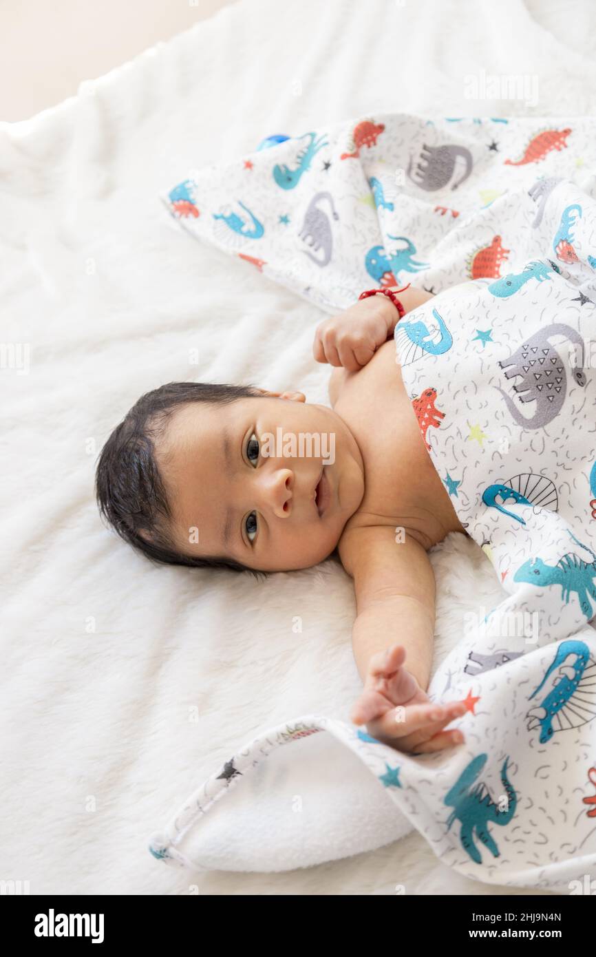 Liegend im Bett mit einer Decke ein lateinisches Baby herumliegend, Unschuld und Zärtlichkeit eines Säuglings, neues Leben und Familienmitglied, Lebensstil Stockfoto
