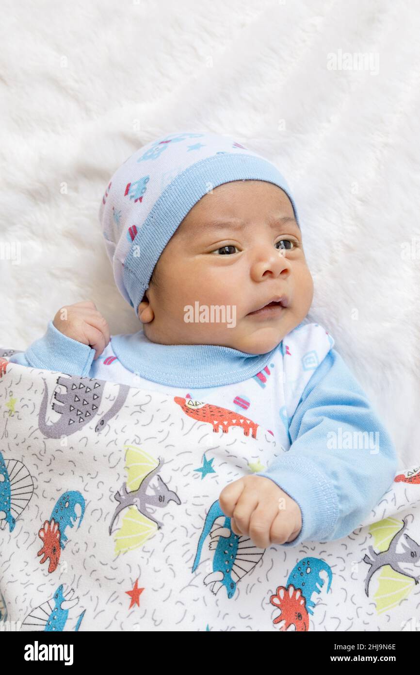 Liegend und warm schönes lateinisches Baby mit offenen Augen und glücklichem Ausdruck, trägt einen Hut und Bettwäsche, neugeborenen Lebensstil, neues Leben und Fürsorge Stockfoto