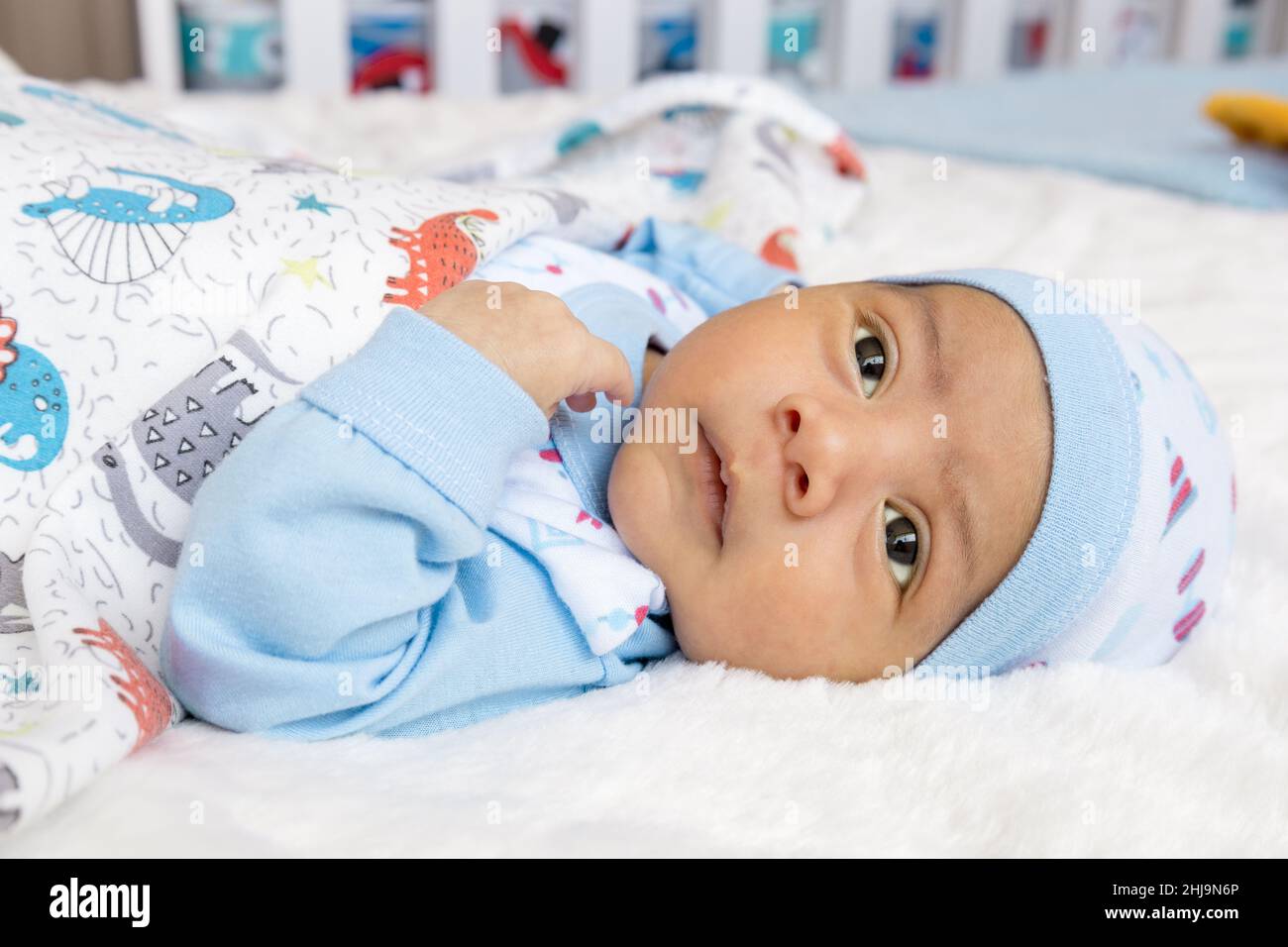 Details zum Gesicht des Babys liegen und mit offenen Augen ruhen, einen Hut und Bettwäsche tragen, neugeborener Lebensstil, neues Leben und Familienmitglied Stockfoto