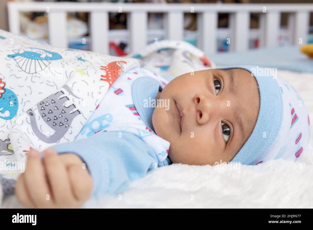 Hübsches Baby, das sich hinlegt und herumschaut, einen Hut und Bettwäsche trägt, einen neugeborenen Lebensstil, ein neues Leben und ein Familienmitglied zu Hause Stockfoto