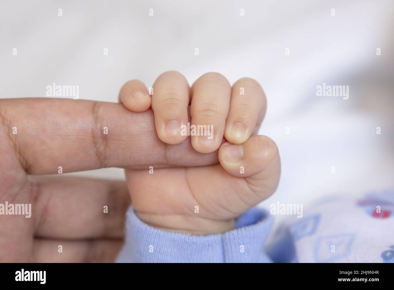 Strukturierte Tapete einer kleinen Hand eines Neugeborenen, die den Finger eines seiner Eltern hält, die Schutz bietet, Unschuld des neuen Lebens, Konzepte der Liebe Stockfoto
