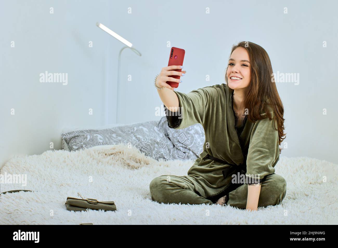 Online-Meeting mit Handy von einer jungen Frau, die im Bett sitzt. Stockfoto