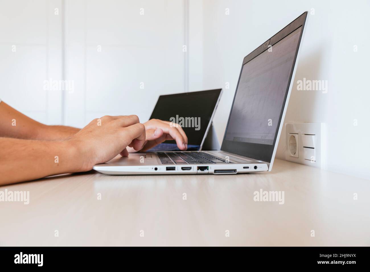 Seitenansicht eines Arbeitsbereichs zu Hause mit zwei Computern, einem an- und einem aus und die Hände eines Mannes, der tippt. Menschen nicht erkennbar. Speicherplatz kopieren Stockfoto