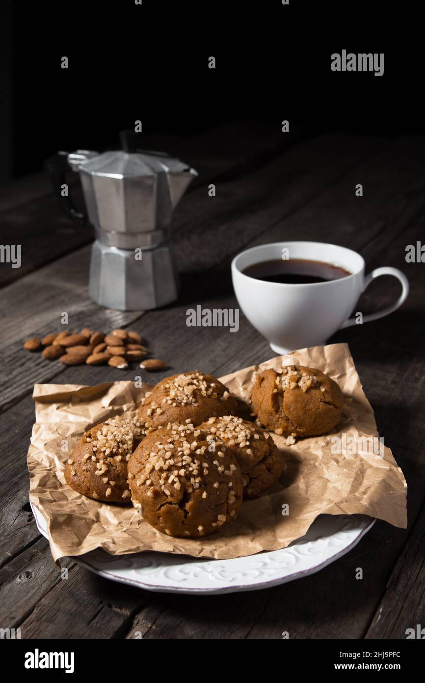 Ein Frühstücksteller aus gebackenen Walnussmuffins, dunklem Kaffee und Mandelnüssen, der auf einer schwarzen Holzplatte platziert ist. Stockfoto