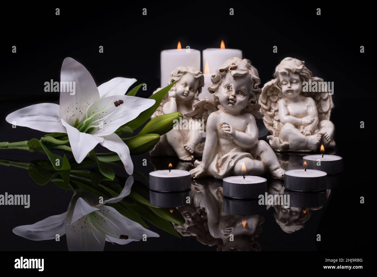 Weiße Engel mit Kerzen und weißer Lilie auf schwarzem Hintergrund. Trauer und Verlust Erinnerung an den Tod Konzept Stockfoto