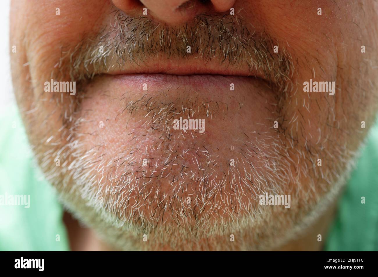 Eine abgeschnittene Aufnahme des Kinns eines Mannes mit schwarzen und grauen Stoppeln. Seine Lippen sind geschlossen, lächeln aber leicht. Seine Nasenlöcher sind nur im Rahmen. Stockfoto