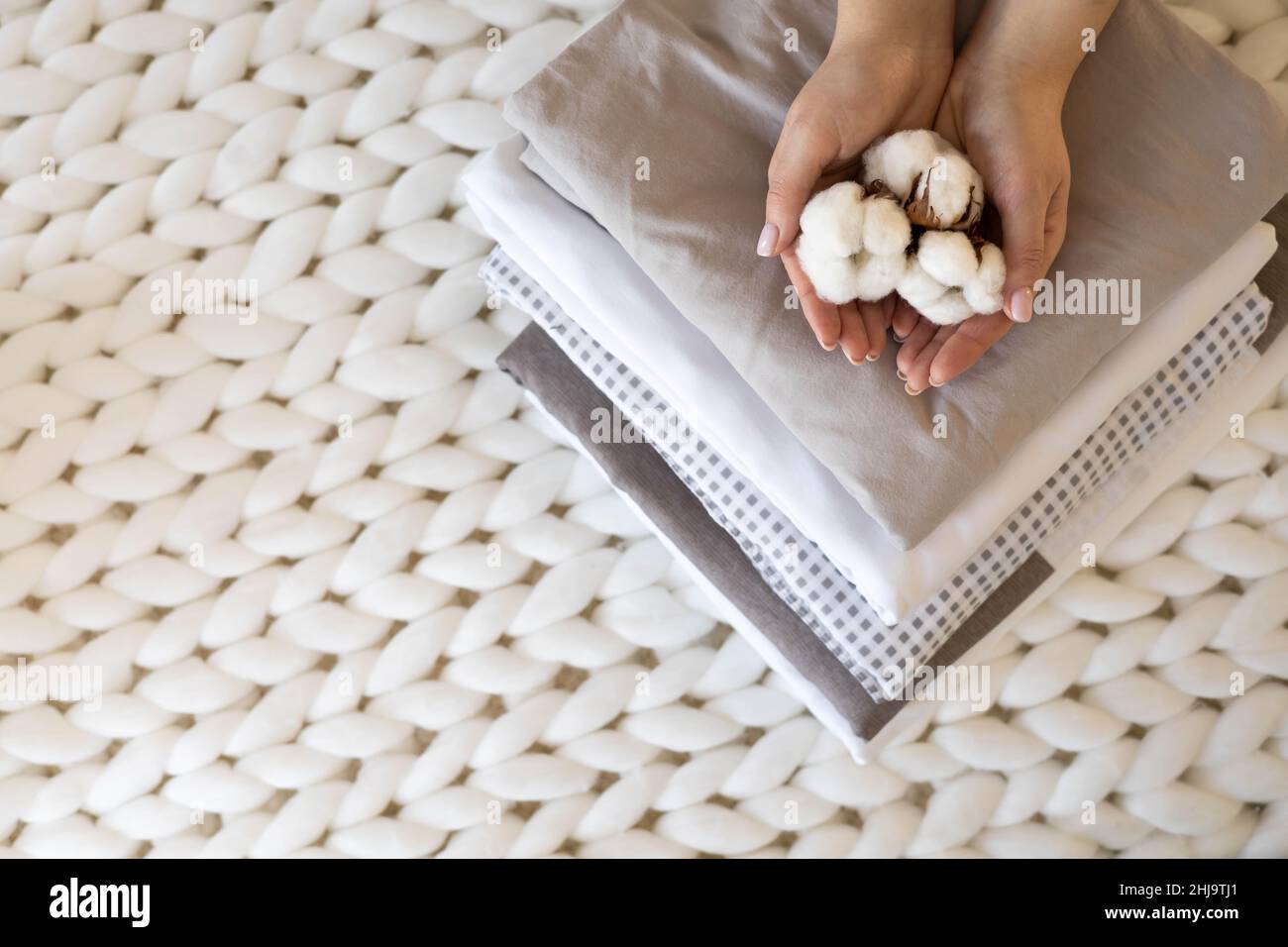 Gut gepflegte Frau Hände halten die Baumwollzweig mit Haufen Von gefalteten Bettlaken und Decken Stockfoto