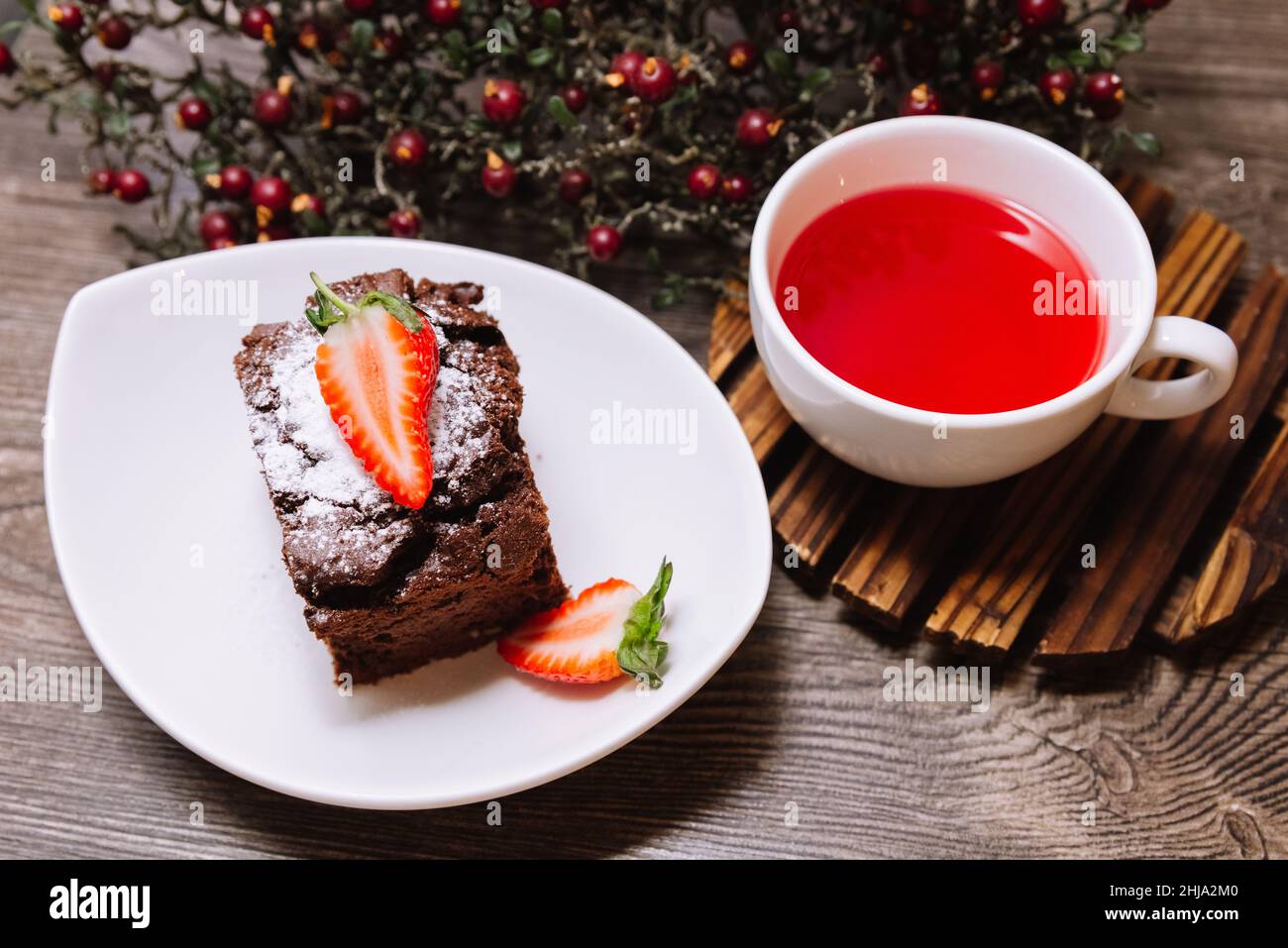 Süßes Dessert mit Erdbeeren. Eine Portion Brownie mit Schokolade und eine Tasse Früchtetee für eine Pause. Auf einer hölzernen Tischplatte. Stockfoto