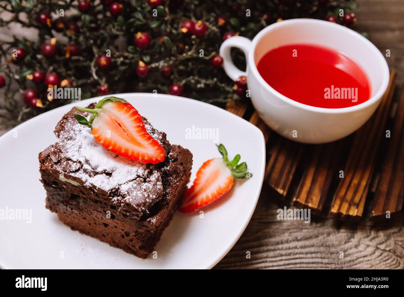 Süßes Dessert mit Erdbeeren. Eine Portion Brownie mit Schokolade und eine Tasse Früchtetee für eine Pause. Auf einer hölzernen Tischplatte. Stockfoto