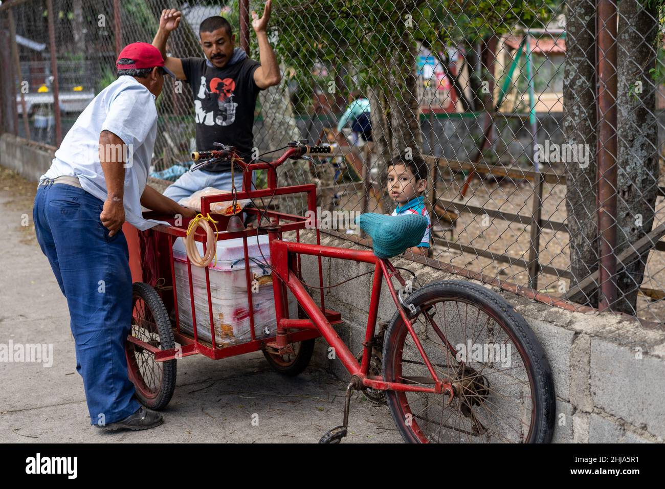 Ein Grundschüler kauft eine Eiskugel von einem Fahrradwagenverkäufer direkt vor dem Schulzaun in Jinotega, Nicaragua Stockfoto