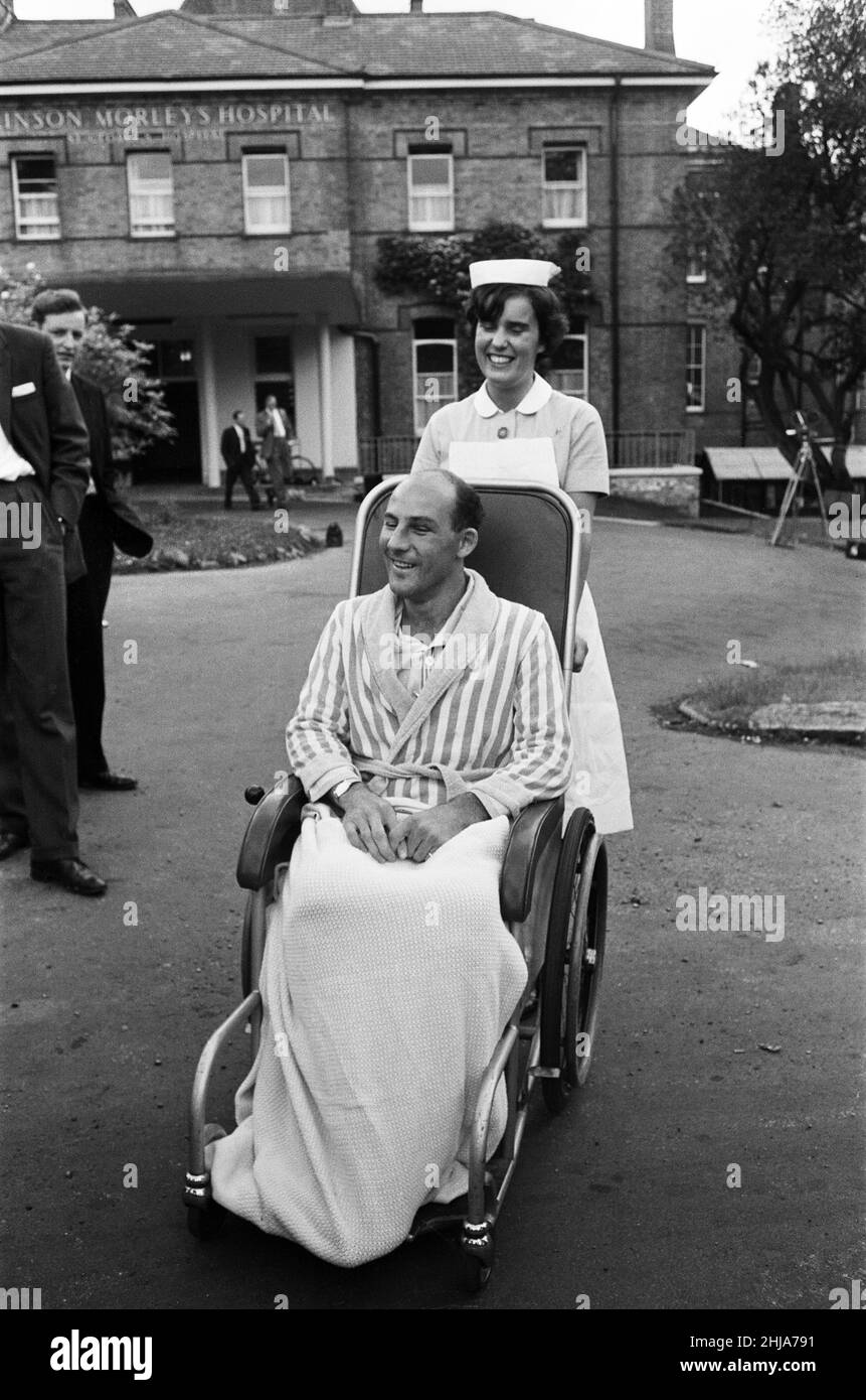 Stirling Moss, abgebildet in einem Rollstuhl, der von einer Krankenschwester geschoben wird, auf dem Gelände des Atkinson Morleys Hospital in Wimbledon. Stirling, 32, erhielt vor sieben Wochen bei einem 120-m.p.h-Unfall in Goodwood Kopf-, Arm- und Beinverletzungen. 11th. Juni 1962. Stockfoto