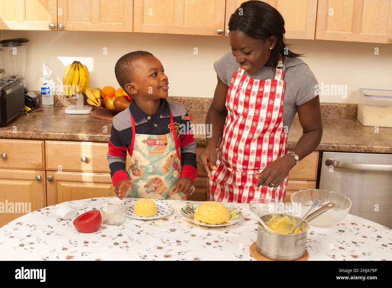 4-jähriger Junge in der Küche zu Hause mit seiner Mutter, nachdem er togalesisches Gericht mit Maismehl 'Fufu' zubereitet hatte, glückliche Interaktion Stockfoto
