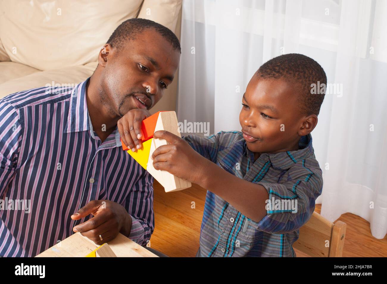 Der 4-jährige Junge spielt mit Holzblöcken, die seinem Vater eine Dreiecksform zeigen Stockfoto