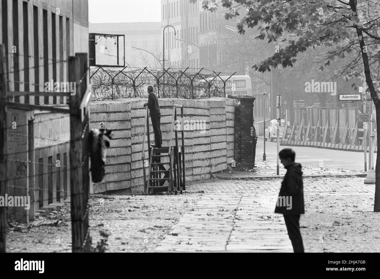 Szenen in Berlin, drei Jahre nach Beginn der Arbeiten am Bau der Berliner Mauer, die Ost und West trennt: Ein West-Berliner Bürger steht über der Berliner Mauer in der Bernauer Straße, einer Straße im französischen Sektor, an der die Berliner Mauer entlang lief. Viele Fluchttunnel wurden unter der Mauer auf der Straße gegraben, darunter der berühmte Tunnel 57, der in der Strelitzer Straße endete. In zwei Nächten im Oktober 1964 gelang es 57 Ostdeutschen, zu entkommen. Aufgenommen am 25th. Oktober 1964. Stockfoto