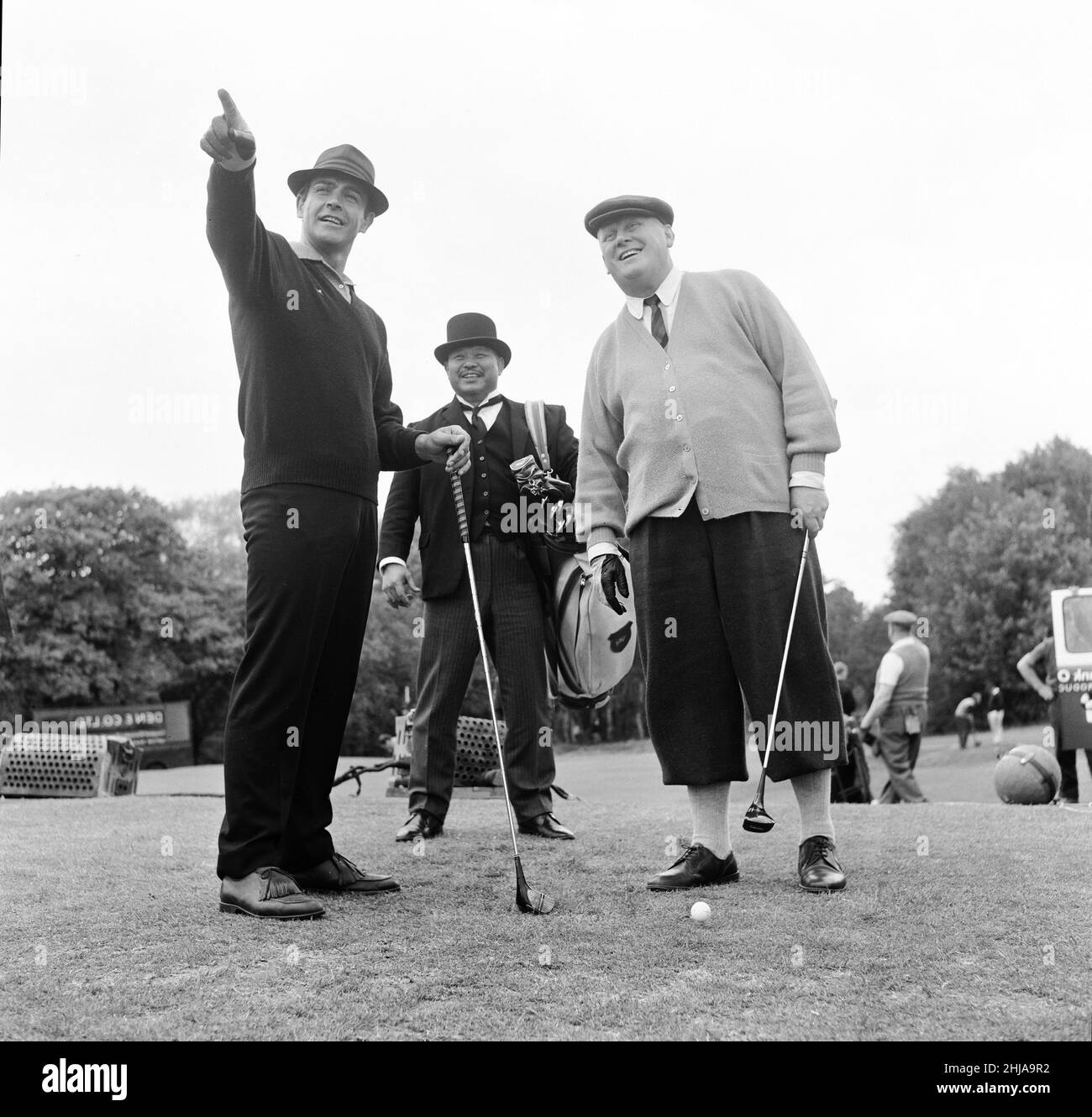 Die Dreharbeiten zur Golfszene für „Goldfinger“ auf dem Golfplatz Stoke Park in der Nähe von Stoke Poges, Buckinghamshire, waren Sean Connery ( James Bond ) Gert Frobe ( Goldfinger ) und Harold T Sakata, besser bekannt als „Tosh Togo“ in der Wrestling World. Harold spielt für diese Szene die Rolle des Caddys.im Film spielen James Bond und Goldfinger für einen £5000-Einsatz. Das Spiel ist von Anfang bis Ende schief, aber Bond gewinnt am Ende Natürlich. 21st Mai 1964 Stockfoto