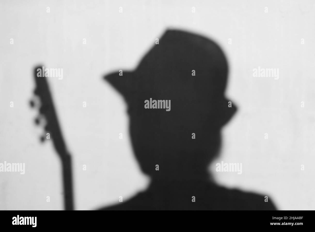 Abstrakte Person Silhouette in Hut und mit Gitarre auf grauem Hintergrund, Musikkonzept. Schwarz und Weiß. Akustikgitarrist. Hobby, Gitarrenunterricht und cou Stockfoto