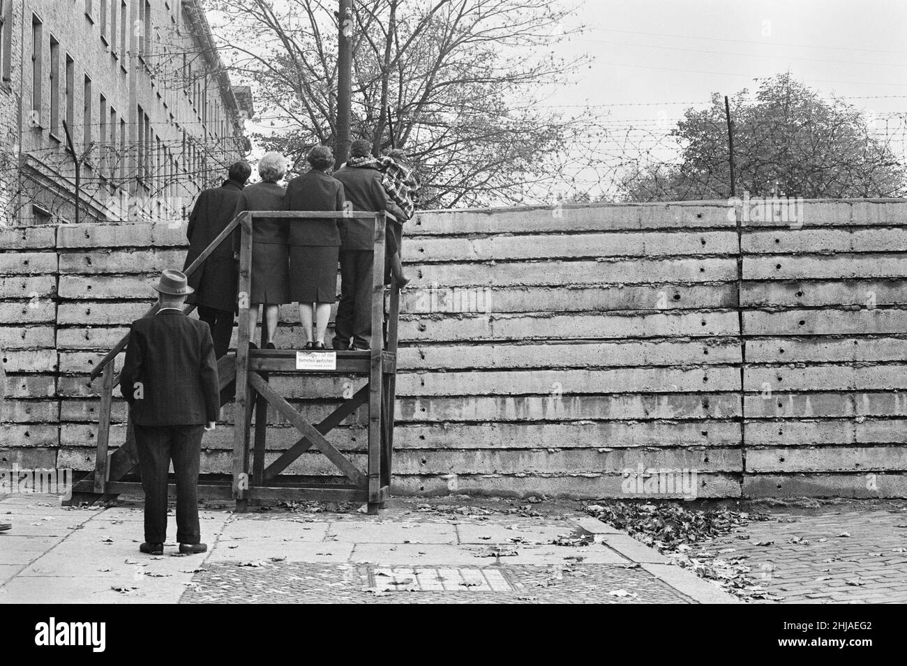 Szenen in Berlin, drei Jahre nach Beginn der Arbeiten am Bau der Berliner Mauer, die Ost und West voneinander trennt.West-Berliner Bürger blicken über die Spitze der Berliner Mauer in der Bernauer Straße, einer Straße im französischen Sektor, an der die Berliner Mauer entlang lief. Viele Fluchttunnel wurden unter der Mauer auf der Straße gegraben, darunter der berühmte Tunnel 57, der in der Strelitzer Straße endete. In zwei Nächten im Oktober 1964 gelang es 57 Ostdeutschen, zu entkommen. Aufgenommen am 25th. Oktober 1964. Stockfoto