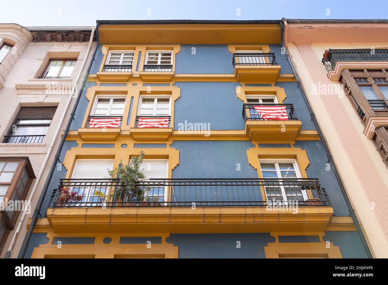 Gelbe Balkone an der Fassade eines Wohngebäudes mit roten und weißen Fahnen in Bilbao. Immobiliengeschäft, klassische Architekturkonzepte Stockfoto