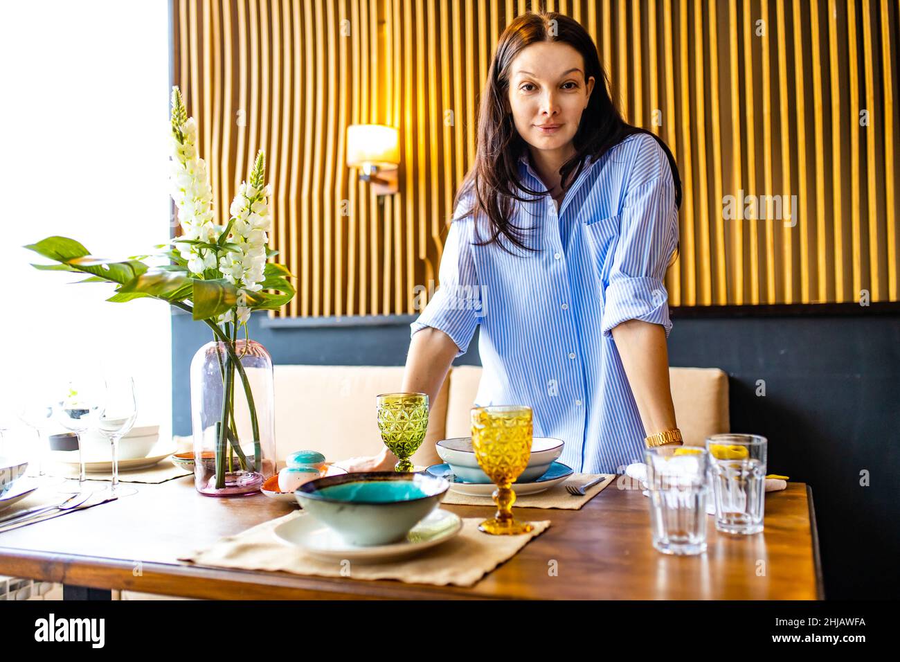 Porträt einer jungen, schönen kaukasischen Frau, die ein Geschirr wascht und den Tisch bei Tageslicht einlegt Stockfoto